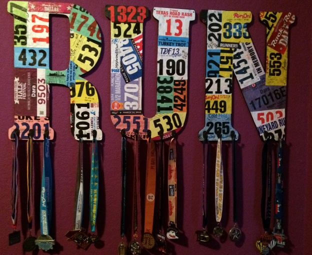 A collection of race medals and bibs arranged to form the word 'DONERUNS', representing a runner's achievements.