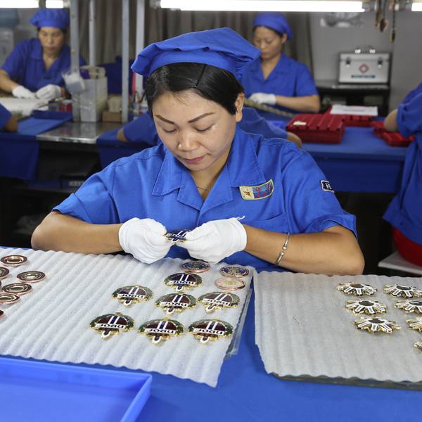 A factory worker conducting a quality inspection on finished metal badges.