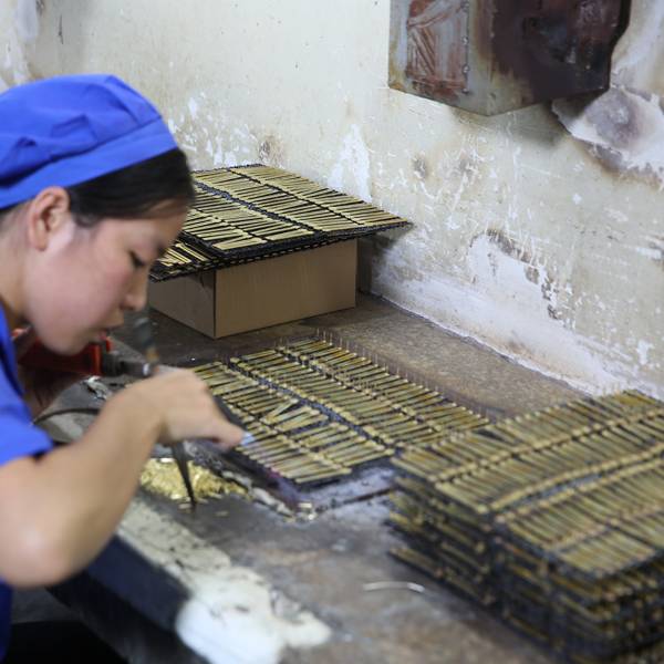 A factory worker carefully assembling small metal parts through silver soldering.