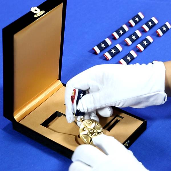 A finished gold medal being carefully packaged with its ribbon.