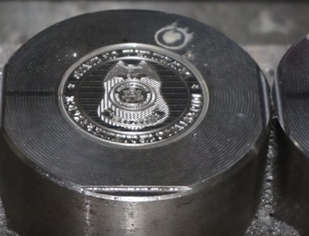 A metal die stamping mold with a detailed circular design for creating custom emblems.
