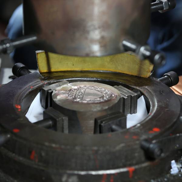 A metal stamping machine in the process of creating a coin or medal.