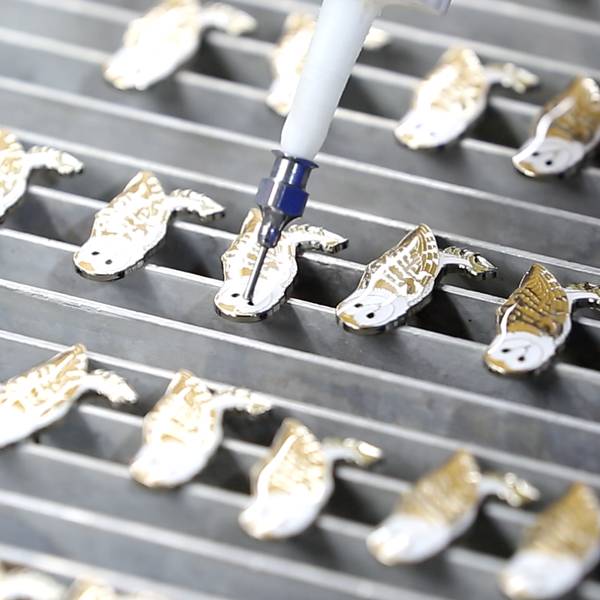 Applying a protective epoxy coating to turtle-shaped metal charms.